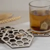 Set van zes houten bijenonderzetters met honingraatmotief en theeglas op linnen doek