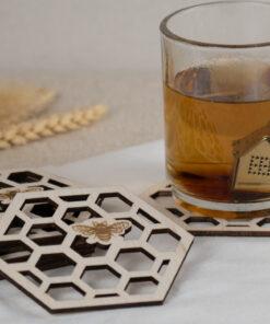 Set van zes houten bijenonderzetters met honingraatmotief en theeglas op linnen doek