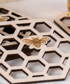 Set van zes houten bijenonderzetters met honingraatmotief en theeglas op linnen doek