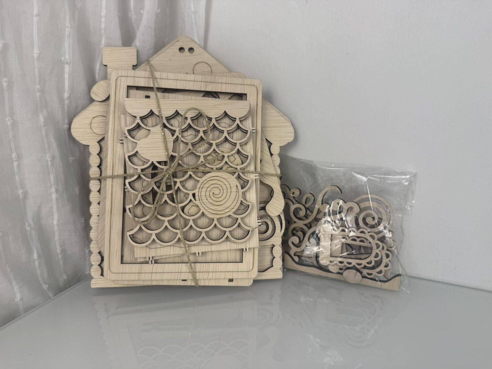 Houten decoratieve huisvorm met gedetailleerde snijwerk en losse onderdelen in een plastic zak.