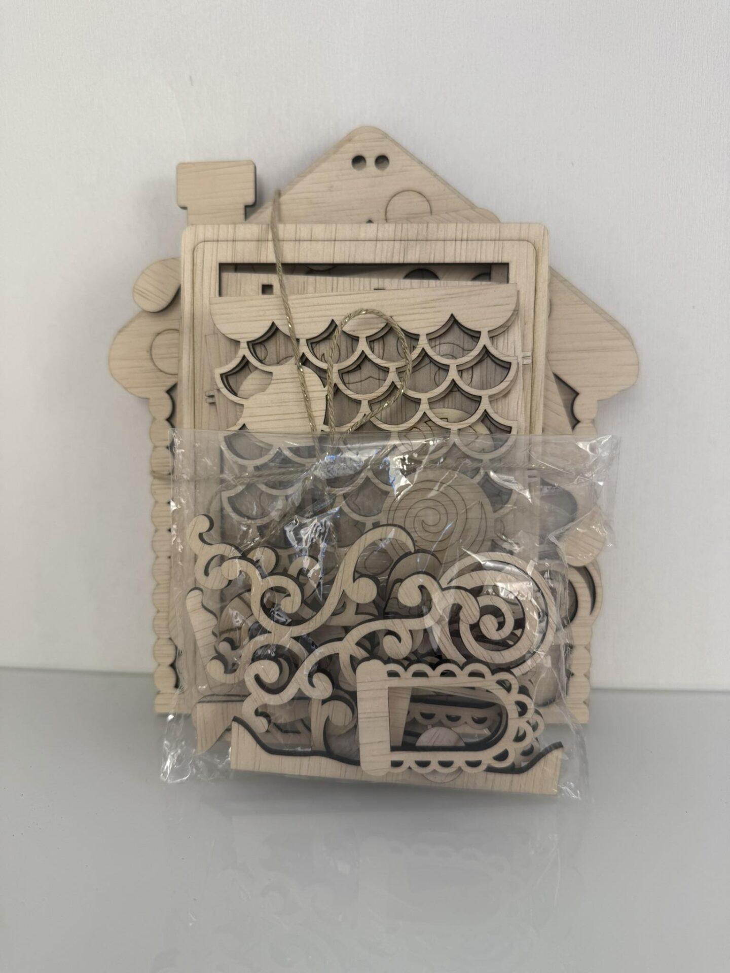 Houten decoratieve elementen verpakt in een doorzichtige zak met een huisvormige achtergrond.