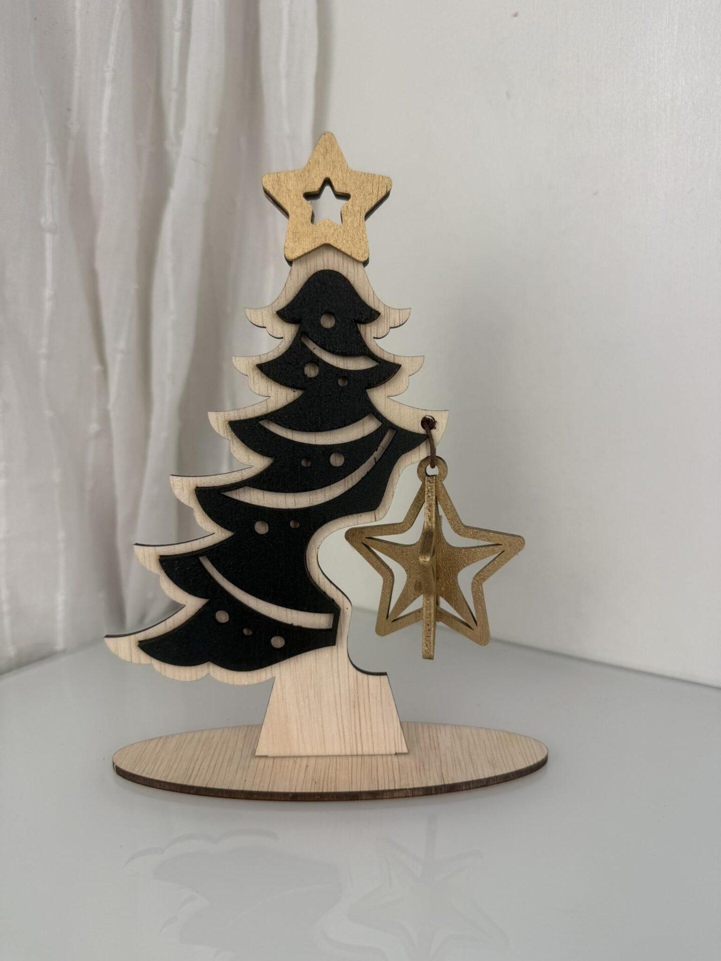Houten kerstboom met een zwarte vorm en een gouden ster ornament aan een tak.
