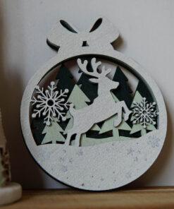 Houten kerstornament met een rendier en sneeuwvlokken, omringd door bomen in een cirkelvormig ontwerp.