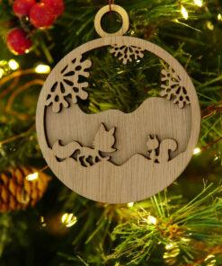 Houten kerstornament met een ontwerp van een vos, eekhoorn en sneeuwlandschap aan een kerstboom.