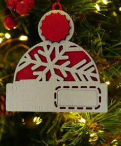 Houten kerstornament in de vorm van een hoed met sneeuwvlok en een label aan een dennenboom.