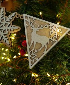 Houten kerstornament in de vorm van een hert en sneeuwvlokken, hangend aan een kerstboom.