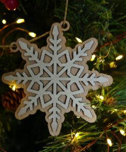 Houten sneeuwvlok ornament hangt aan een kerstboom met verlichting.
