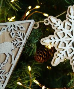 Houten ornamenten in de vorm van een rendier en een sneeuwvlok, hangend aan een kerstboom.