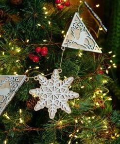 Houten kerstdecoraties in de vorm van een sneeuwvlok en driehoekige vormen aan een kerstboom met verlichting.